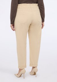 Béžové kalhoty s vysokým pasem, elastickým pasem, zúženými nohavicemi, ohrnutými manžetami a dvěma zadními kapsami, doplněné o nahé lodičky na vysokém podpatku.