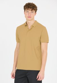 Khaki polo skjorta i mjukt tyg, med klassisk krage, tre-knappars placket och korta ärmar. Diskret logotyp på bröstet.