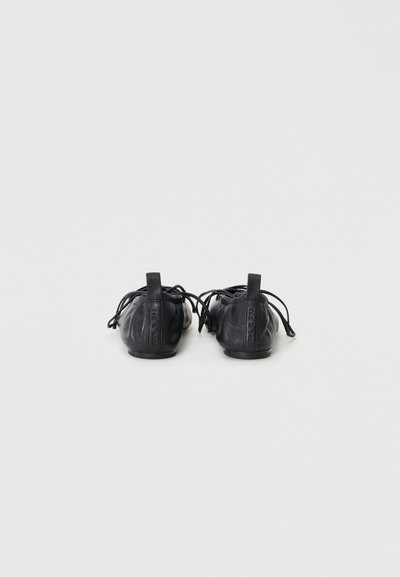 Bottines en cuir noir avec une semelle plate, des lacets et des tirettes à l'arrière, présentant un design supérieur texturé. Style minimaliste, sans marque visible.