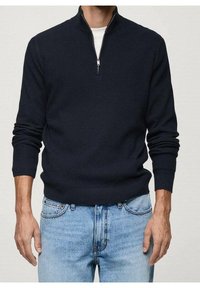 Maglione blu navy a coste con collo a mezza zip, maniche lunghe e vestibilità rilassata, abbinato a jeans in denim azzurro chiaro.