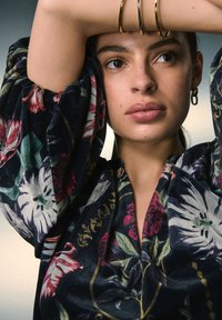 Top in tessuto a motivo floreale con sfondo blu navy intenso, maniche oversize e tessuto morbido. Dettagli con bracciale dorato e orecchino a cerchio.