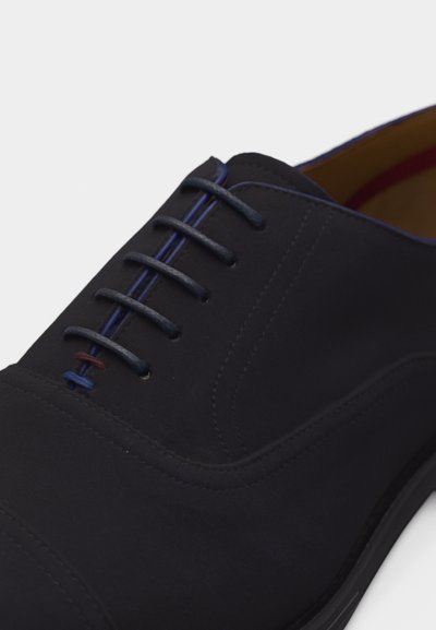 Μαύρο δερμάτινο παπούτσι φορέματος με κλειστό κορδόνι, μπλε περιμετρική ρίγα κατά μήκος της γλώσσας και διακοσμητική ραφή σε μπλε και καφέ κοντά στις κάτω τρύπες για κορδόνια.