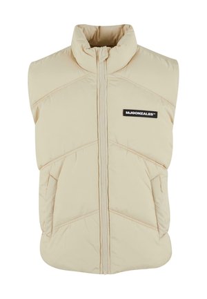 Beige padded vest with high collar, front zip, diagonal stitching, and a black logo patch on the left chest. Soft, quilted texture.