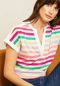 Juostuota trumpomis rankovėmis palaidinė rožinės, žalios, geltonos ir baltos spalvų, su V formos iškirpte ir minkšta, lengva medžiaga. Dėvima su mėlynais džinsais.