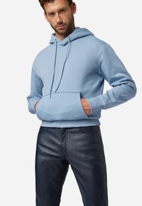 Lichtblauwe hoodie van zacht materiaal, met een voorzak, trekkoorden en geribbelde manchetten, gecombineerd met een donkere leren broek.