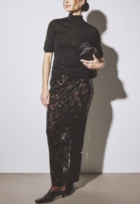 Maglione corto a maniche corte nero abbinato a una gonna nera con paillettes e un motivo testurizzato, completato da una borsa a tracolla nera e scarpe a punta.