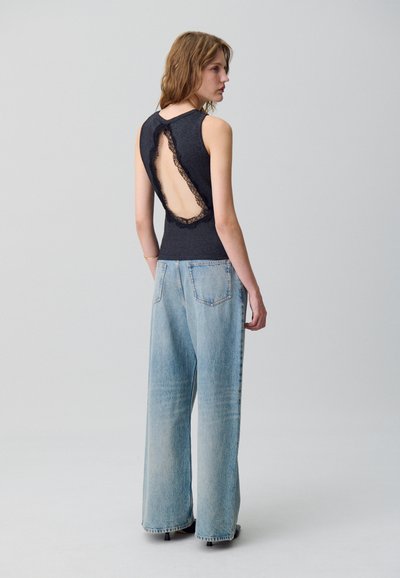 Top negro sin mangas con detalles de encaje en la espalda abierta, combinado con jeans de pierna ancha en azul claro. Textura suave, silueta casual.