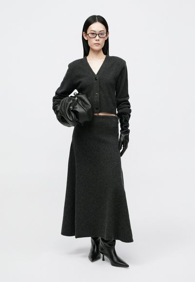Σκούρος γκρι πλεκτός κάρντιγκαν με κουμπιά, σε συνδυασμό με μια μακριά φούστα στο ίδιο χρώμα. Τα αξεσουάρ περιλαμβάνουν μια μαύρη δερμάτινη τσάντα χειρός και γάντια, μαζί με εφαρμοστά τακούνια.