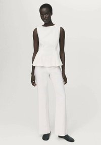 Top peplum bianco abbinato a pantaloni bianchi a gamba dritta. Tessuto liscio e strutturato con una silhouette elegante e un design minimal. Scarpe nere.