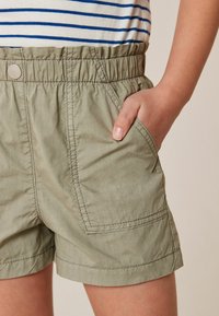 Ljus olivgröna shorts med elastisk midja, framficka och kontrasterande sömmar. Texturerat tyg med en avslappnad design.