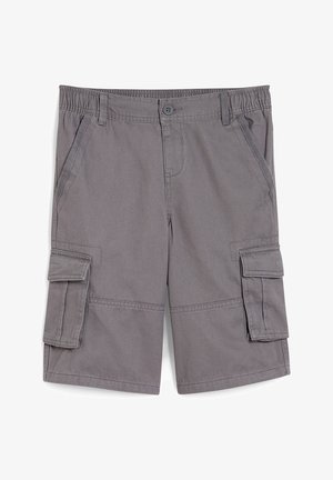 Barn iført en sort PlayStation-t-shirt, grå cargobukser, hvide sokker med sorte striber og sorte og hvide sneakers, stående mod en hvid væg.
