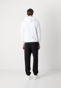 Hanorac alb cu șnur și mânici zimțate, asortat cu pantaloni negri de trening și adidași albi. Design simplu, fără modele vizibile.