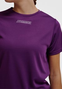 Lila sport-t-shirt i texturerat tyg med korta ärmar och rund halsringning. "HUMMEL"-logotypen är broderad på bröstet.