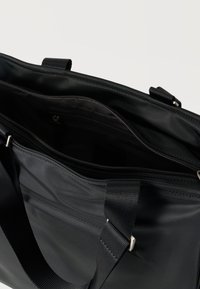 Μαύρη τσάντα φορητού υπολογιστή από νάιλον με φερμουάρ, υφασμένους ιμάντες και εσωτερικές τσέπες. Διαθέτει λείο φινίρισμα και μινιμαλιστικό σχέδιο.