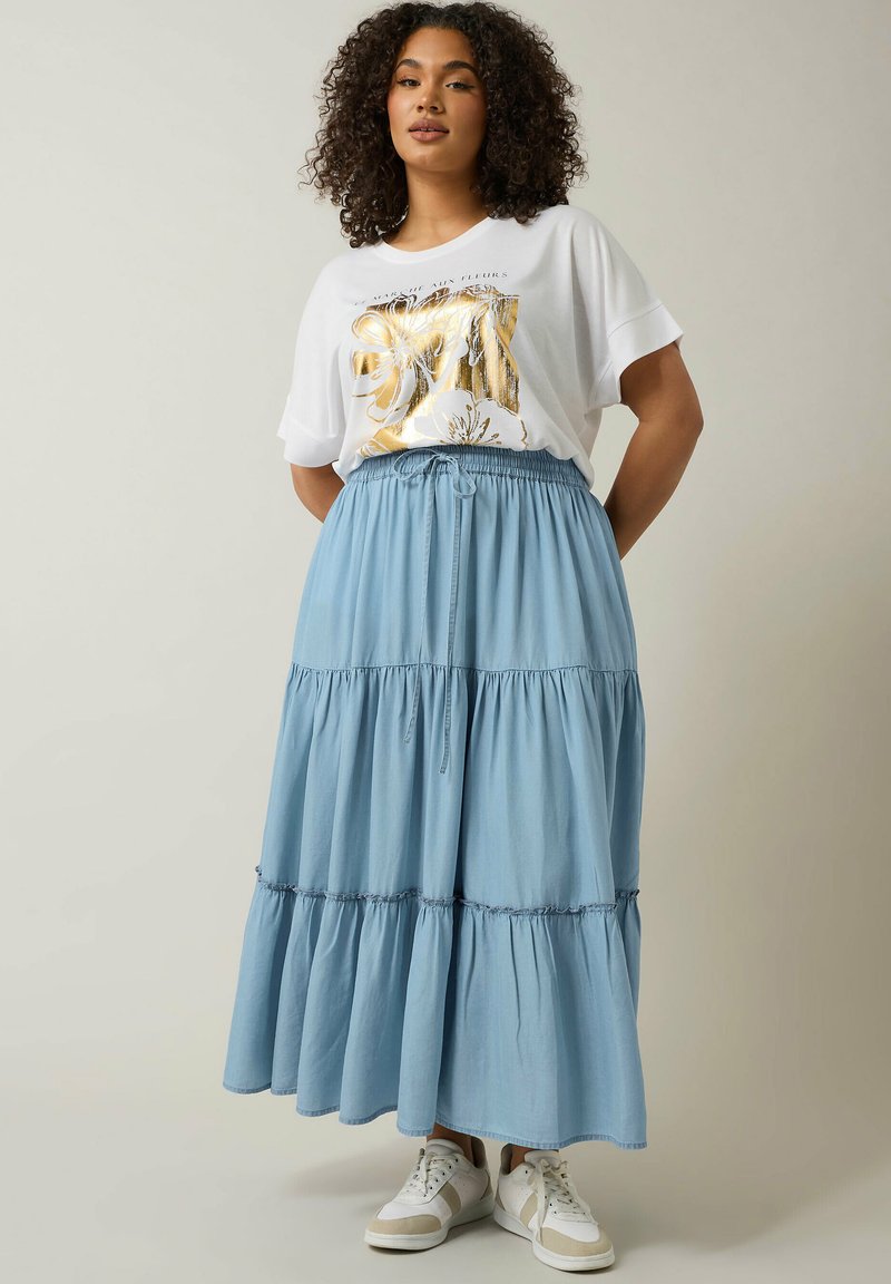 Gonna maxi a strati di colore azzurro chiaro con vita elastica e coulisse. Abbinata a una maglietta bianca con una grafica floreale dorata. Sneakers bianche.