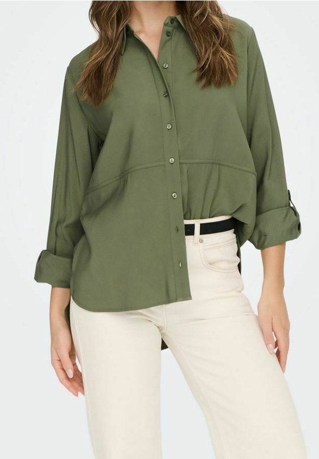 Femme portant une chemise ample vert olive boutonnée avec manches retroussées et un pantalon taille haute écru avec une ceinture noire.