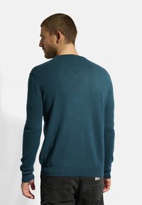 Tyrkysový pletený svetr s dlouhými rukávy, kulatým výstřihem a žebrovanými manžetami a lemem. Disponuje texturovanou látkou a volným střihem.