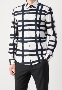 Chemise à manches longues noire et blanche avec un motif à carreaux brossé audacieux, dotée d'une fermeture à boutons sur le devant et aux poignets, associée à un pantalon noir.