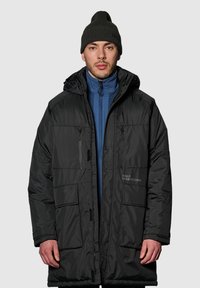 Czarna kurtka puchowa z kapturem, z niebieską wewnętrzną warstwą, wieloma przednimi kieszeniami i zapięciami na zamek. Obecne mankiety ściągane i szczegóły z logo.