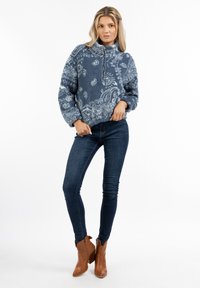 Fleece pullover i mørkeblå med paisley mønster, med design til lynlås i halsen, elastiske manchetter og en afslappet pasform. Bæres med mørke jeans.