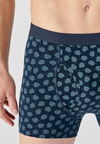 Pantaloni boxer in tessuto blu scuro con motivo a foglia in blu chiaro. Vita elastica con una texture liscia. Design con tasca frontale.