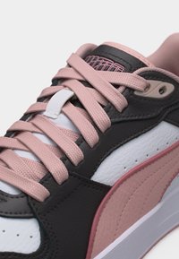 Κοντινή εικόνα ενός αθλητικού παπουτσιού με ροζ κορδόνια, μαύρες και λευκές δερμάτινες επιφάνειες και ροζ ρίγα στη μία πλευρά.