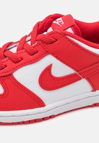 Red and white athletic shoe with a leather and mesh upper, featuring padded collar, round toe, laces, and a prominent red Nike swoosh logo.