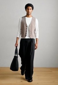 Γκρι γιλέκο πάνω από λευκό πουκάμισο με μακριά μανίκια, μαύρο παντελόνι με φαρδιά σκέλη και μαύρη τσάντα tote. Λείες υφές και ουδέτεροι τόνοι.