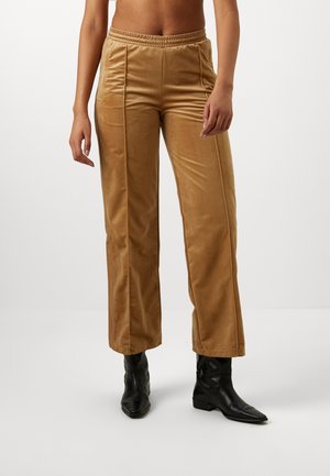 Pantalon en velours beige avec jambes droites, coutures avant et taille élastique, porté avec des bottines noires à bout pointu par une personne debout.
