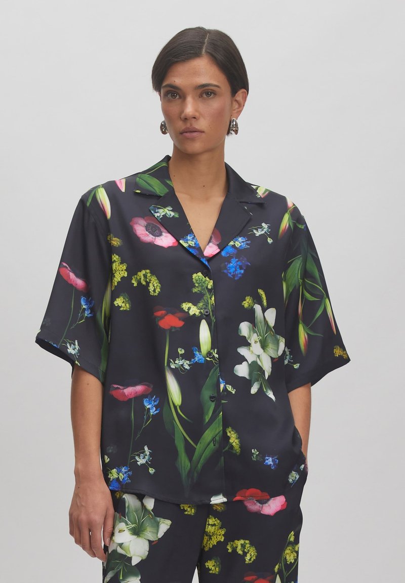 Kurzarmhemd aus schwarzem Stoff mit einem lebhaften Floralprint, der rote, rosa, blaue und grüne Blumen zeigt, und einem lockeren Schnitt.