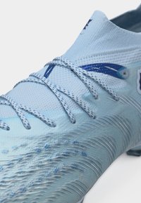 Svijetloplavi kopački za nogomet s teksturiranim gornjim dijelom, ušivenim vezicama i djelomičnim tamnoplavim logotipom u području gležnja.