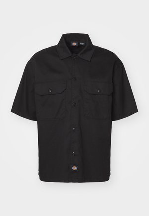 Camisa negra de manga corta con cierre de botón, dos bolsillos en el pecho y un cuello redondeado. Fabricada con un material duradero, presenta un pequeño detalle de logo.