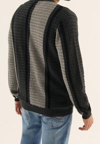 Maglione lavorato a maglia con un motivo testurizzato in grigio e nero, caratterizzato da strisce verticali e maniche lunghe, abbinato a jeans blu chiaro.