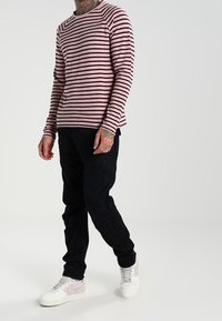 Gestreiftes Langarmshirt in Pink und Schwarz, kombiniert mit dunkler Hose und weißen Sneakern. Verfügt über einen runden Ausschnitt und eine gerippte Textur.