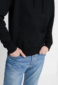 Zwarte katoenen sweatshirt met capuchon en geribde boorden, gecombineerd met lichtblauwe denim jeans. Focus op een relaxte pasvorm en een soepele textuur.