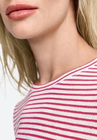 Juostuota palaidinė su horizontaliais rožiniais ir baltais dryžiais. Minkšta medžiaga, apvaliu kaklu ir raukšlėta tekstūra. Detali nuotrauka, kurioje matomas apykaklės ir lūpų artėjimas.