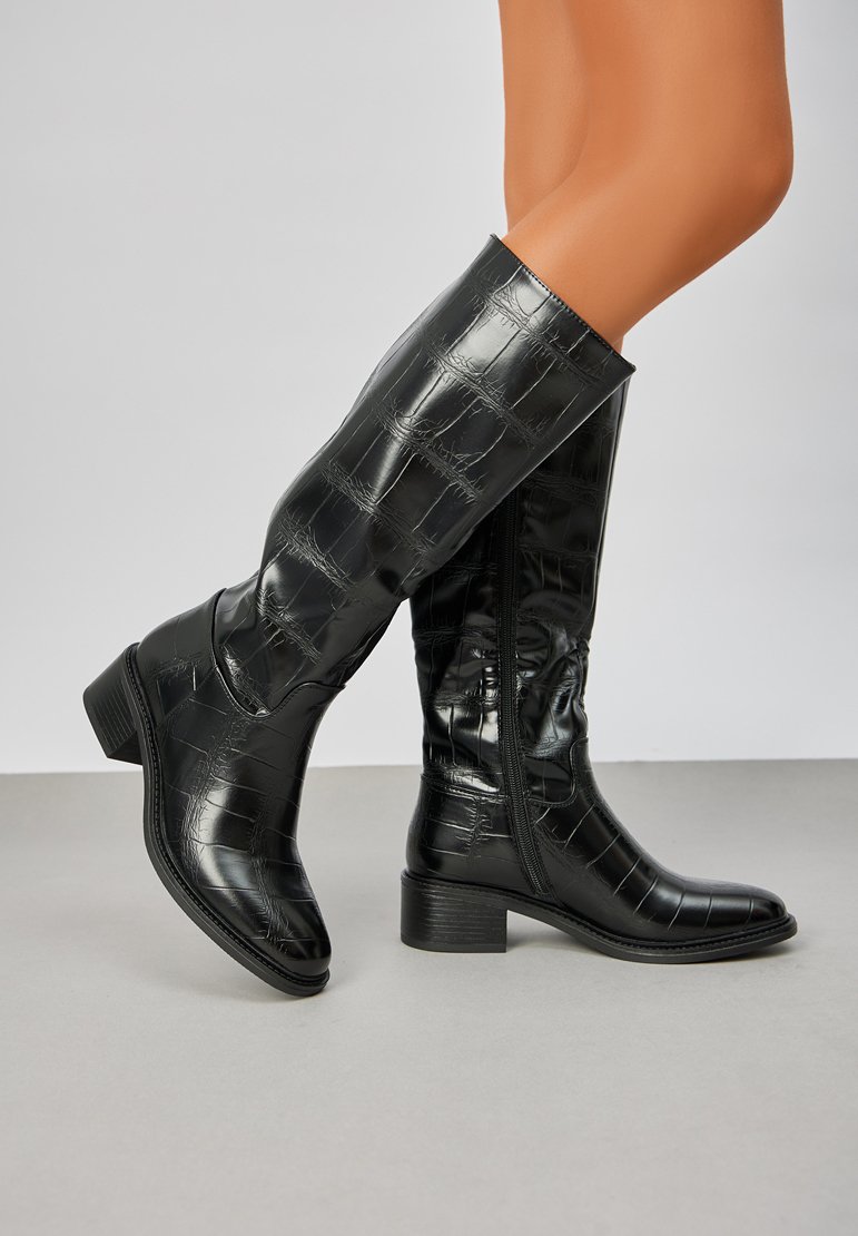 Bottes noires montantes en matériau verni embossé crocodile, dotées d'un talon bloc modéré et d'une fermeture éclair sur le côté pour un enfilage facile.