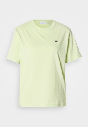 Hellgelbes Baumwoll-T-Shirt mit rundem Ausschnitt, kurzen Ärmeln und kleinem grünem Lacoste-Logo auf der Brust. Einfaches Design und weiche Textur.