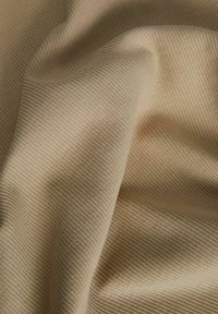 Tissu beige côtelé avec des plis doux et une texture, montrant de fines lignes verticales et un drapé naturel.