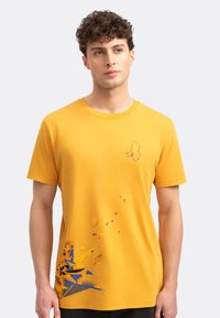 Geel katoenen t-shirt met een grafisch ontwerp met blauwe en oranje accenten. Ronde halsstijl met korte mouwen en een losse pasvorm.