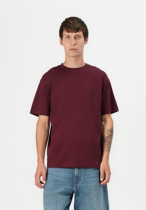 Burgundy t-shirt med kort ärm och rund halsringning, tillverkad av mjuk bomull, ihop med ljusblå denimjeans. Har en avslappnad passform och enfärgad design.