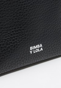 Czarna torba z fakturowanej skóry z wyraźnie umieszczonym białym logo "BIMBA Y LOLA" w nowoczesnej czcionce bezszeryfowej.