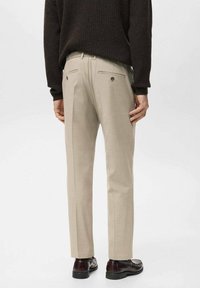 Pantalones beige a medida con ajuste recto, dos bolsillos traseros con botones y una textura suave, combinados con un suéter oscuro y zapatos.