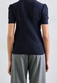Top de punto azul marino con mangas cortas, que presenta un patrón texturizado de líneas verticales y bordes acanalados, combinado con pantalones de vestir grises.