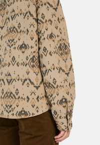 Beige gestreept shirt met diamanten en driehoeken in bruine en zwarte tinten, voorzien van een knoopsluiting bij de manchetten en een licht gebogen zoom.
