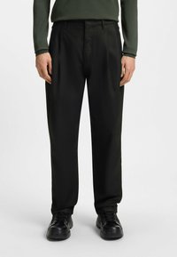 Black trousers with a loose fit, featuring a smooth texture and front pockets, paired with simple black sneakers.