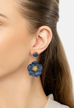 Blue floral earrings feature a textured design with a gold center, hanging from a blue stud. The materials create a vibrant, dimensional look.