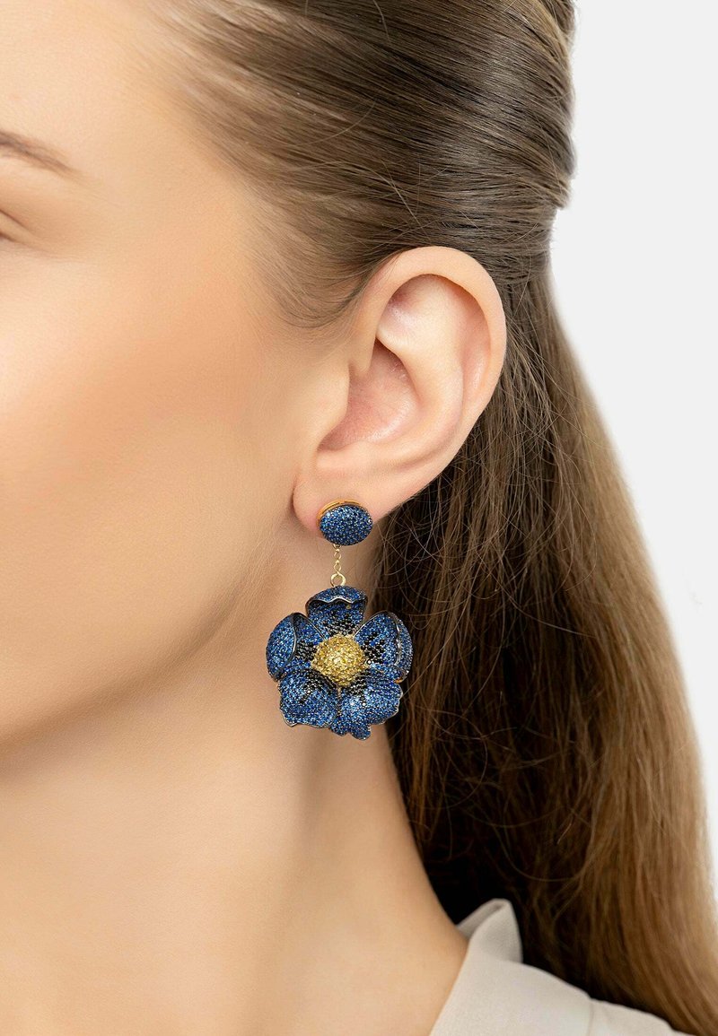 Blue floral earrings feature a textured design with a gold center, hanging from a blue stud. The materials create a vibrant, dimensional look.