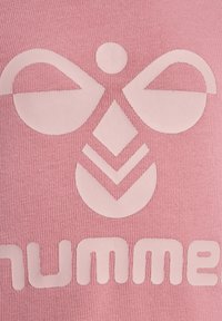 Rosa tyg har en texturerad yta med en ljus logodesign, inklusive symmetriska former och ett geometriskt mönster.