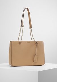 Sac fourre-tout en cuir tanné couleur noisette avec des anses en chaîne et cuir, forme rectangulaire, logo en relief, étiquette amovible et texture lisse.